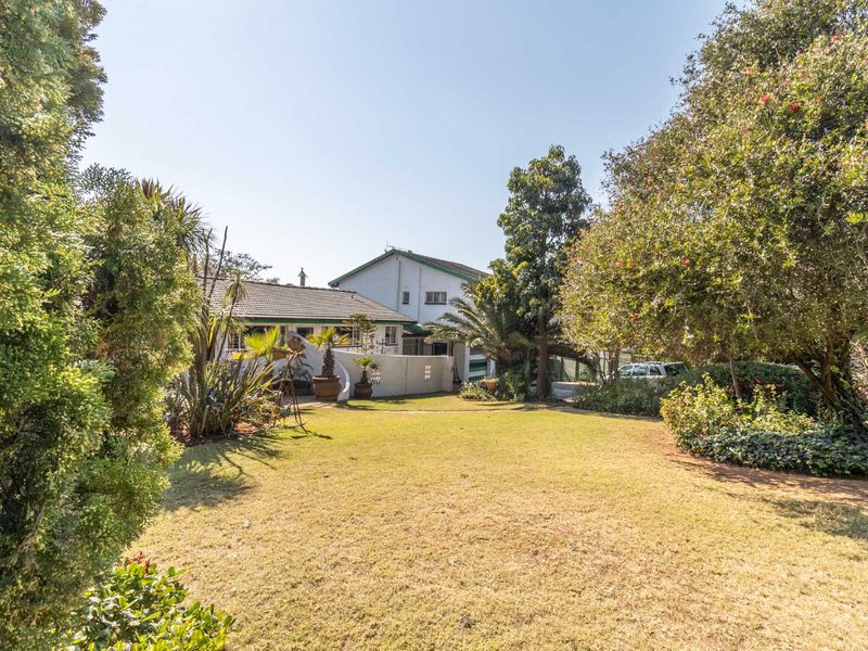 A view of the rear garden featuring a spacious lawn, mature trees, and the rear elevation of the house with a tiled roof.