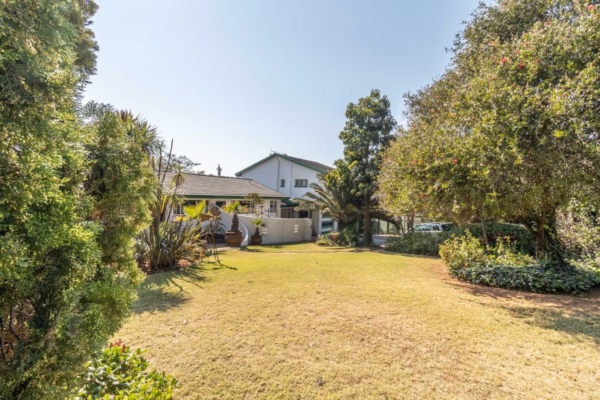 A view of the rear garden featuring a spacious lawn, mature trees, and the rear elevation of the house with a tiled roof.