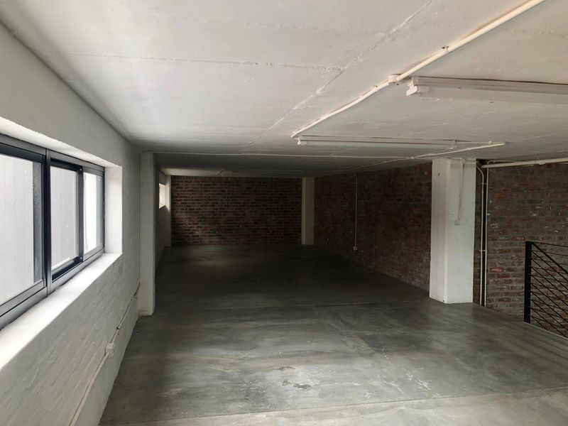 An expansive, empty utility space featuring industrial-style exposed brick walls, polished concrete flooring, and exposed ceiling with integrated lighting.