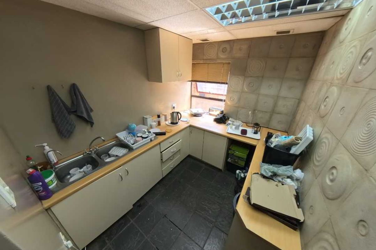 A compact office kitchenette featuring laminate cabinetry, a double basin sink, and textured wall panels under a drop ceiling.