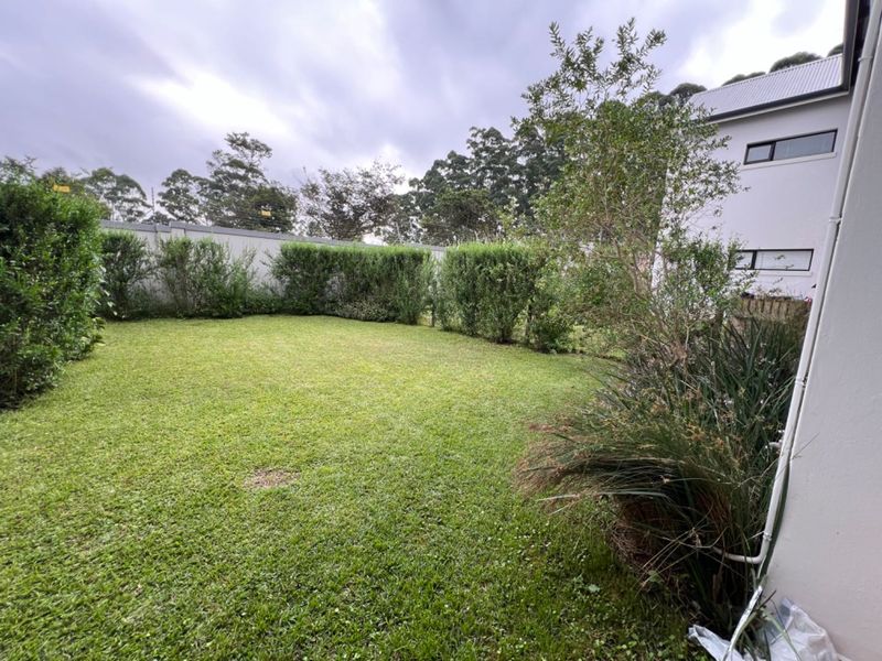 A private rear garden featuring a well-maintained lawn, established perimeter hedging, and a boundary wall.
