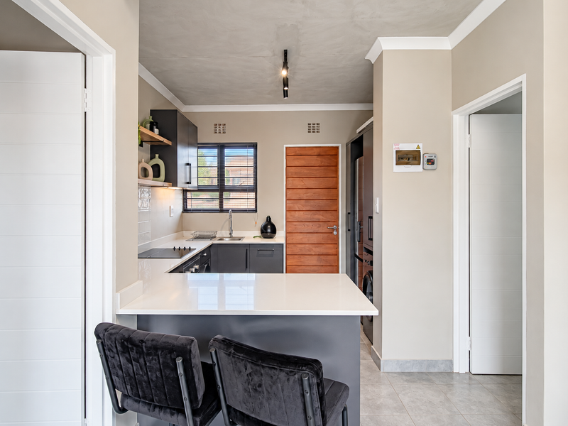 Modern kitchen featuring sleek dark cabinetry, white quartz countertops, an electric hob, and a breakfast bar, complemented by neutral tones and tiled flooring.