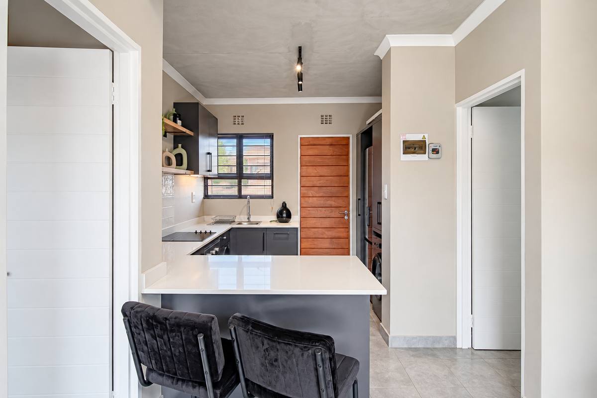 Modern kitchen featuring sleek dark cabinetry, white quartz countertops, an electric hob, and a breakfast bar, complemented by neutral tones and tiled flooring.