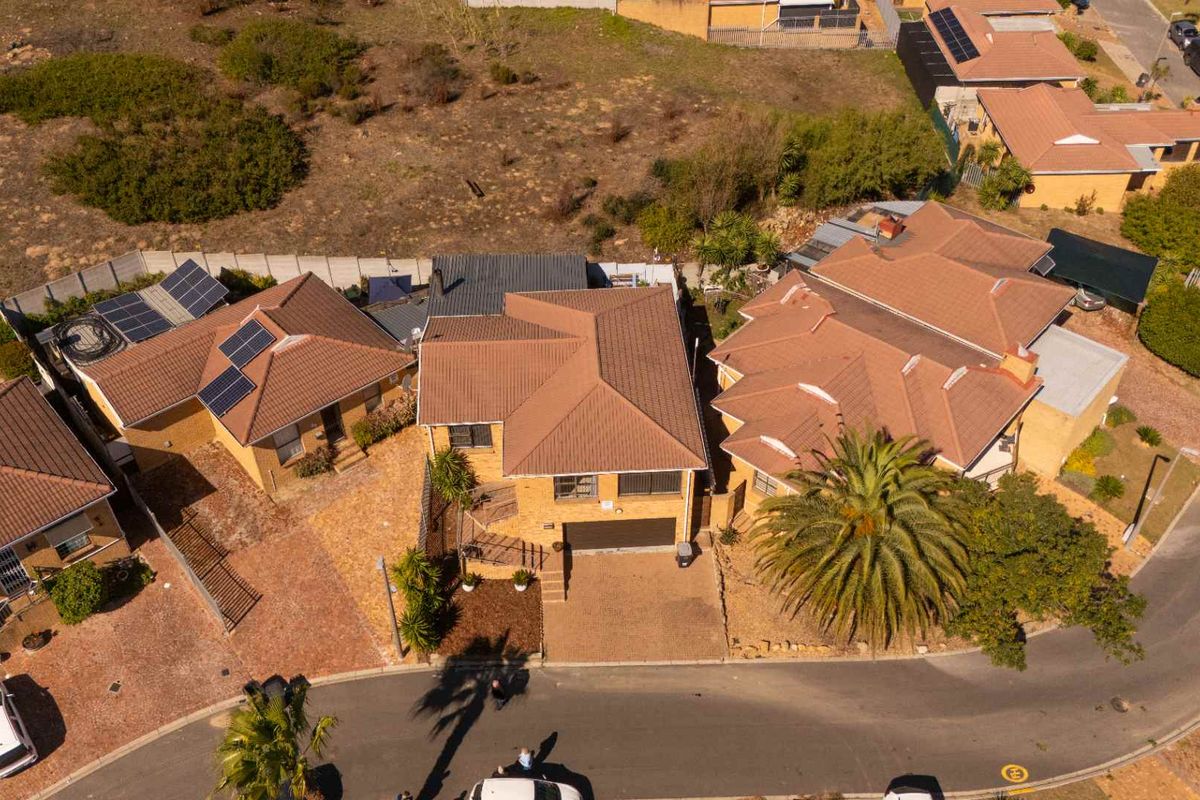 Aerial view of a residential property featuring a tiled roof, paved driveway, and integrated garage within a suburban street setting.