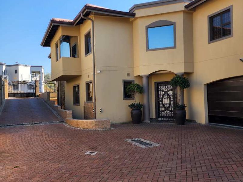 Front elevation of a multi-story residential property featuring a paved driveway, integrated garage, and secure entrance gate.