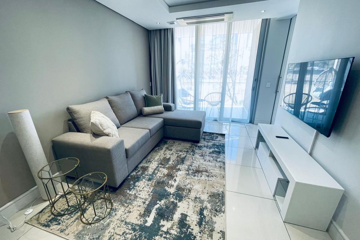 A modern, well-maintained living room featuring sleek tiled flooring, recessed ceiling lighting, and a large sliding glass door providing access to the balcony.