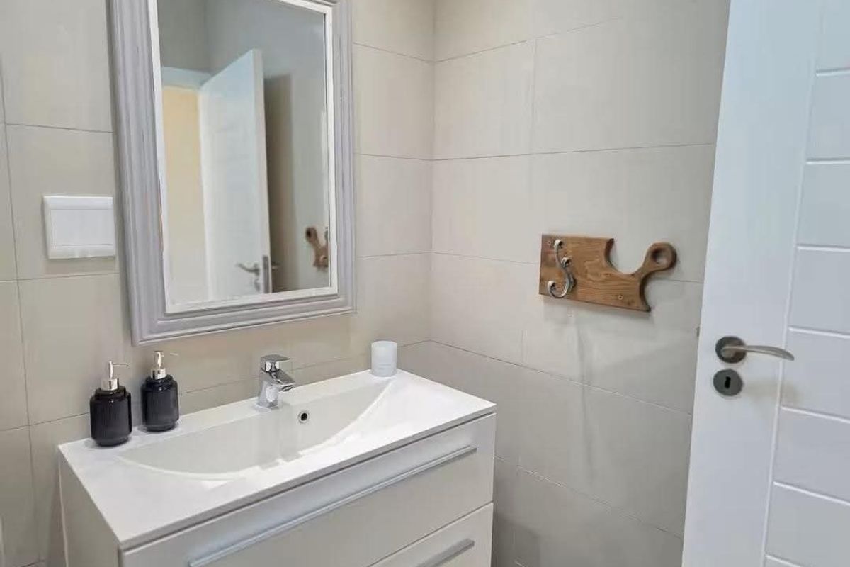 A modern bathroom featuring a sleek white vanity cabinet with a ceramic basin, chrome mixer tap, and a framed wall-mounted mirror.
