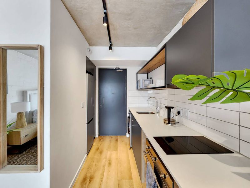 Modern galley kitchen featuring sleek dark cabinetry, stone countertops, integrated appliances, subway tile backsplash, and stylish track lighting against an exposed concrete ceiling.
