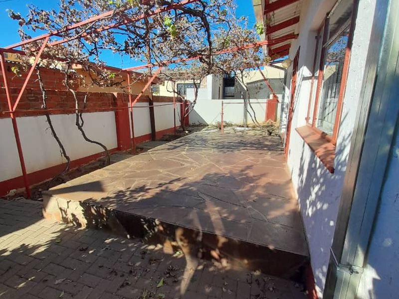 An outdoor patio area featuring stone paving, a metal pergola structure, and a brick boundary wall, offering potential for a refreshed entertainment space.