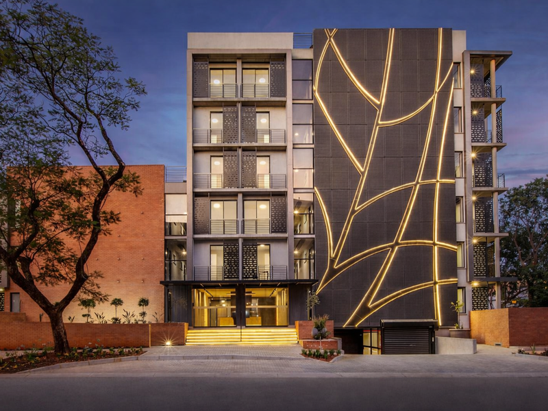 Modern apartment building facade featuring striking decorative metal cladding with integrated lighting, private balconies, and a secure paved entrance area.