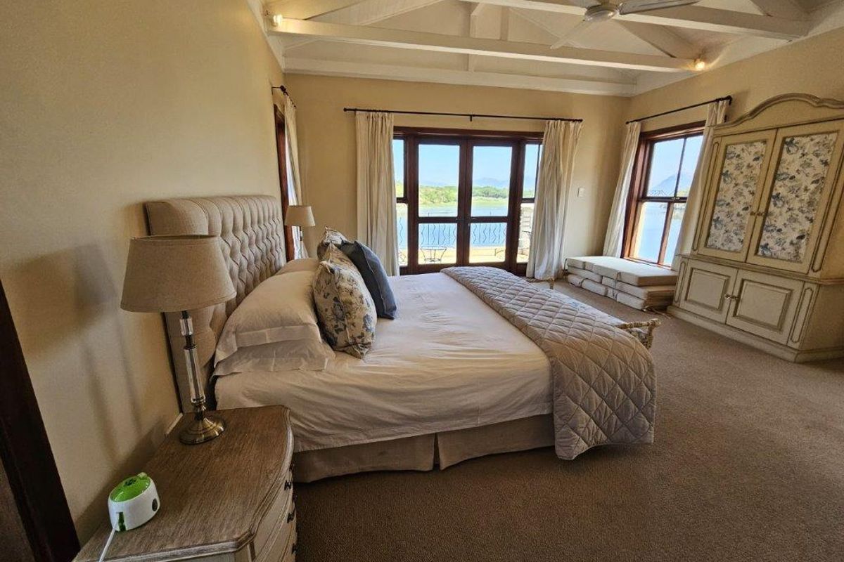 Spacious bedroom featuring vaulted ceilings with exposed beams, carpeted flooring, and large windows offering scenic water views.
