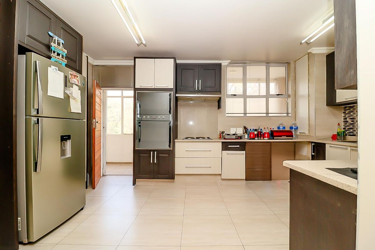 Modern kitchen featuring two-tone cabinetry, stone countertops, built-in oven, gas hob, and tiled flooring with direct access to an adjacent balcony.