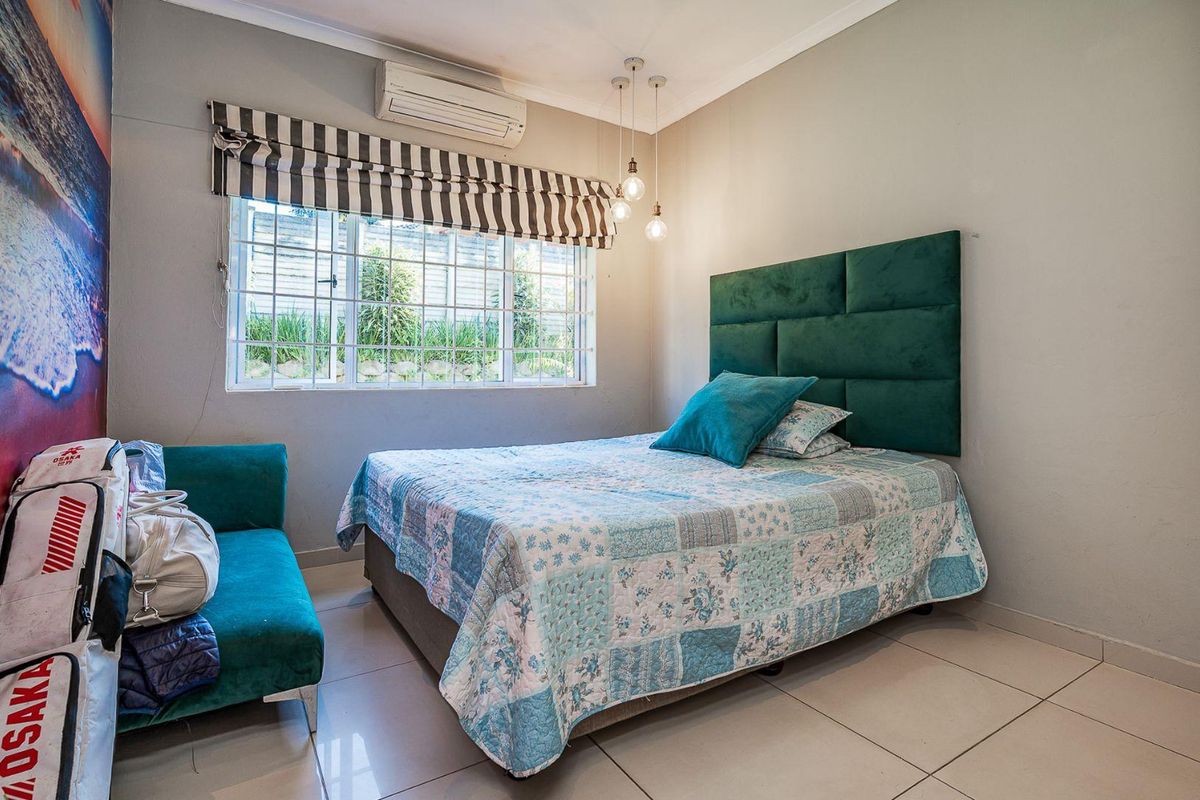A bedroom featuring tiled flooring, a wall-mounted air conditioning unit, and a window with security bars.