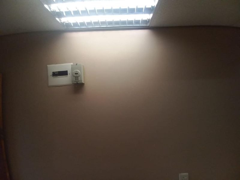 A plain office interior featuring a fluorescent ceiling light, security alarm keypad, and electrical distribution board mounted on the wall.
