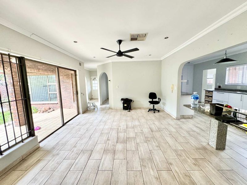 Spacious open-plan living and kitchen area featuring modern tiled flooring, a ceiling fan, and direct access to the outdoor patio through sliding glass doors.