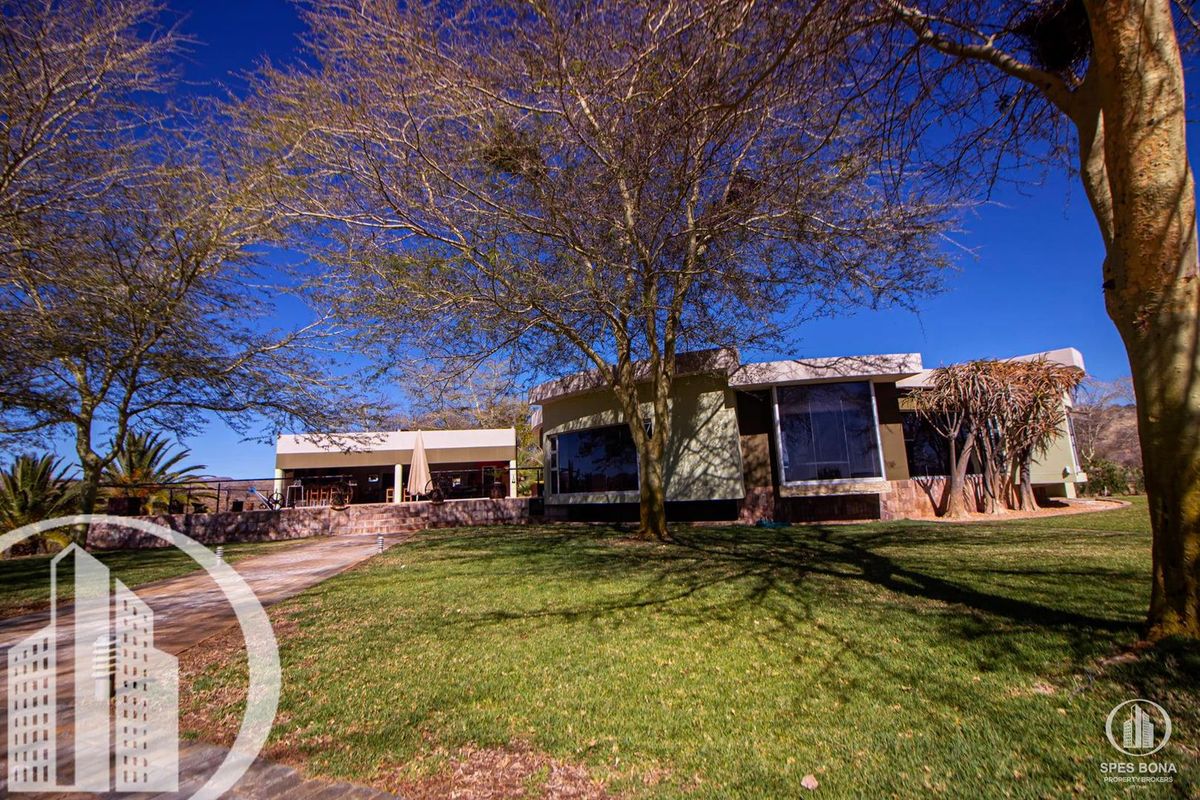 A view of the rear exterior of the house, featuring a landscaped lawn, mature trees, and a paved patio area.