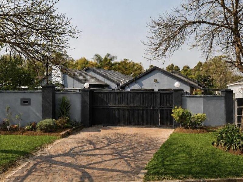 Front view of the property featuring a paved driveway, secure perimeter wall with a sliding gate, and a well-maintained garden.