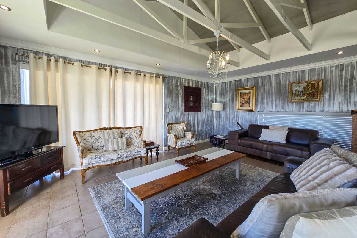 Spacious living room featuring a high vaulted ceiling with exposed trusses, tiled flooring, and large windows with integrated blinds.