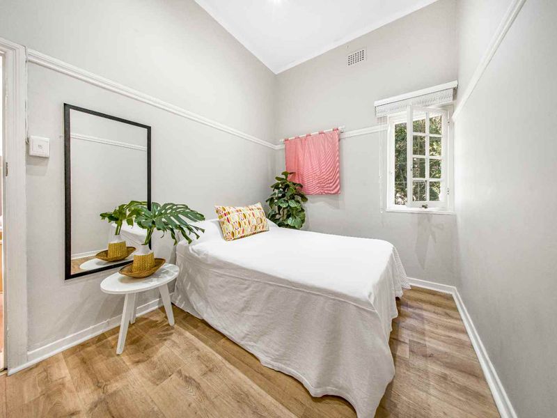 A bright bedroom featuring laminate flooring, a classic picture rail, and a casement window providing natural light.