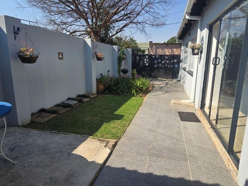 A private rear courtyard featuring a tiled patio area, a small lawn, and a secure boundary wall with a metal gate.