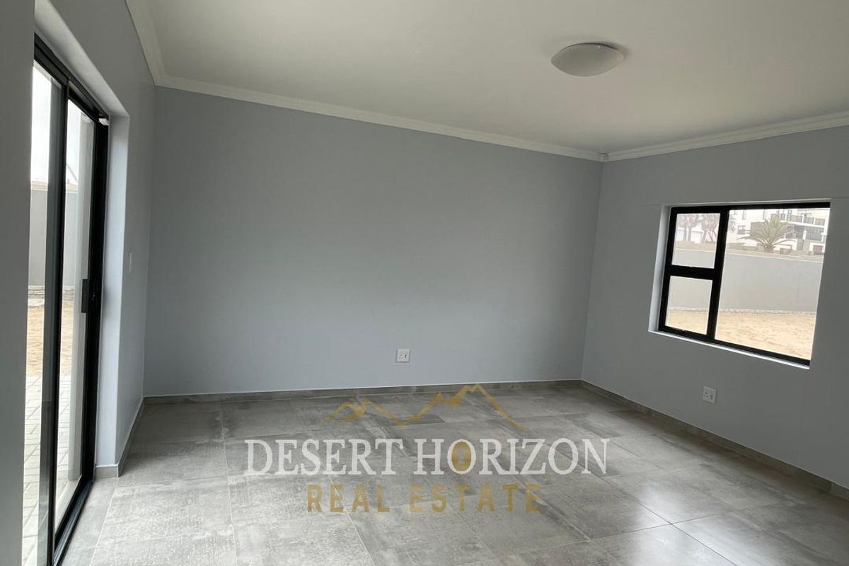 A bright, empty living area featuring large format floor tiles, modern black-framed windows, and sliding glass doors leading to the exterior.