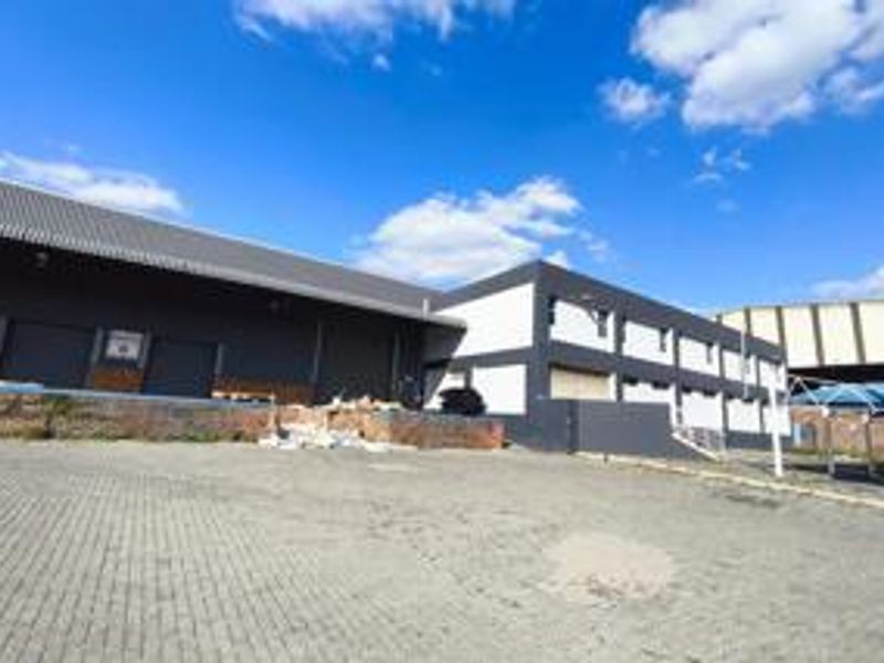Industrial warehouse facility featuring a paved yard, multiple roller shutter doors, and a loading bay area with modern metal cladding.