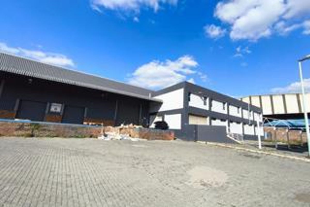 Industrial warehouse facility featuring a paved yard, multiple roller shutter doors, and a loading bay area with modern metal cladding.