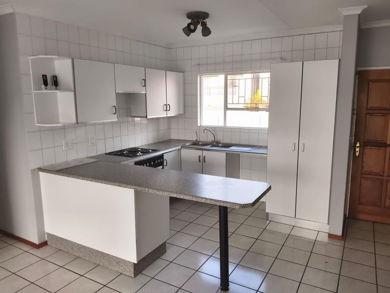 A functional, empty kitchen featuring white cabinetry, laminate countertops, a built-in hob and oven, and tiled flooring with a neutral backsplash.