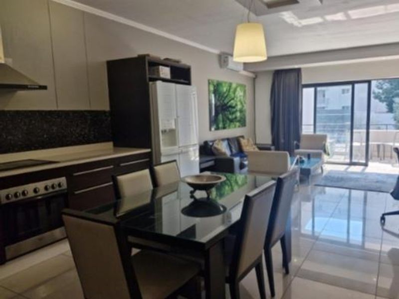 Modern open-plan living area featuring a sleek kitchen with built-in appliances, tiled flooring, and large sliding doors leading to an outdoor balcony.