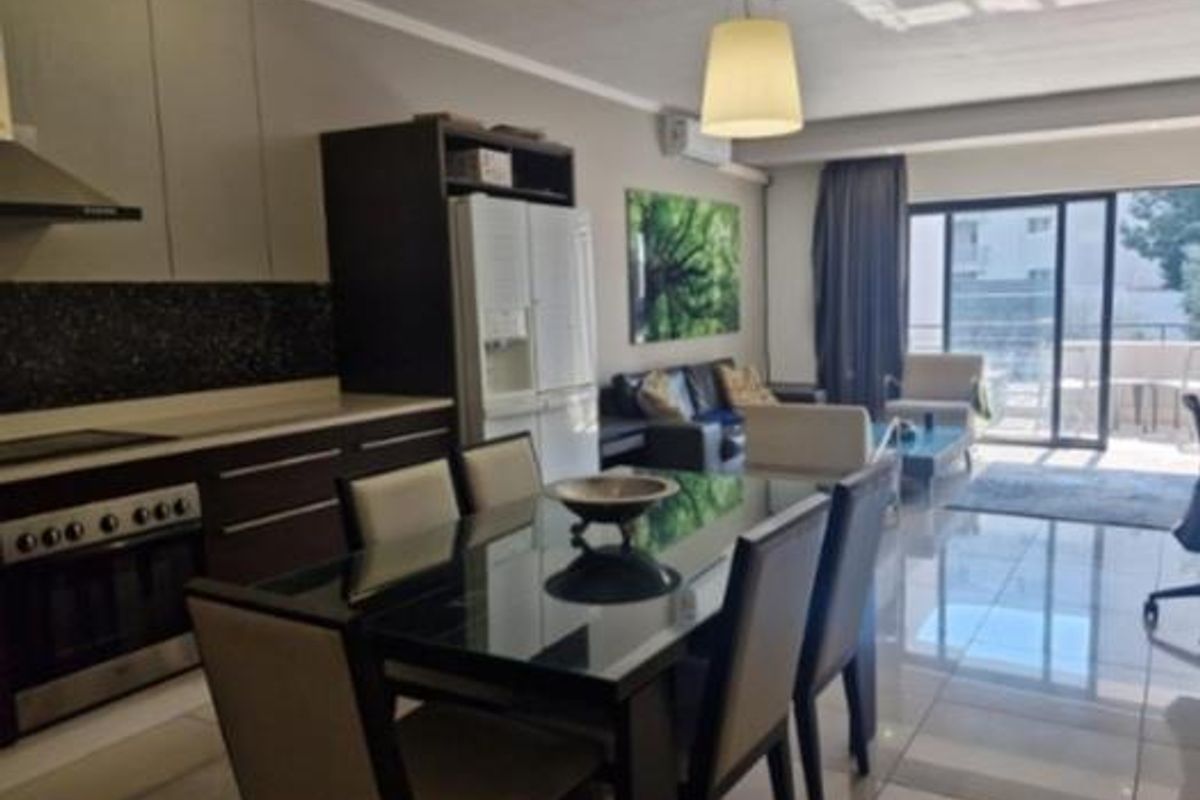 Modern open-plan living area featuring a sleek kitchen with built-in appliances, tiled flooring, and large sliding doors leading to an outdoor balcony.