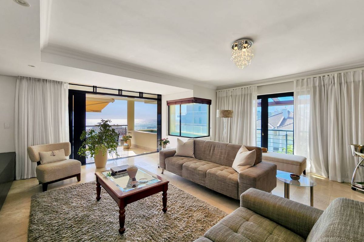 Spacious living room featuring stone flooring, recessed ceiling lighting, and large sliding glass doors opening onto a balcony with ocean views.