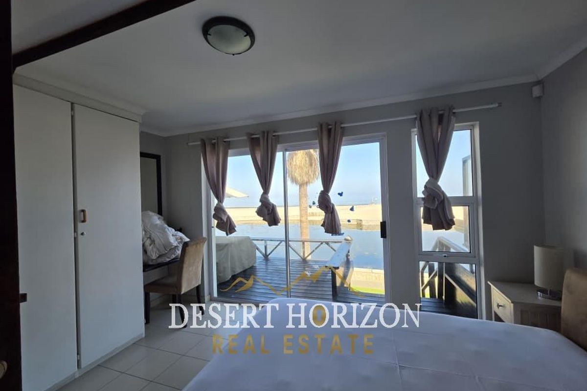 A bedroom featuring built-in cupboards and sliding glass doors that open onto a wooden deck with water views.