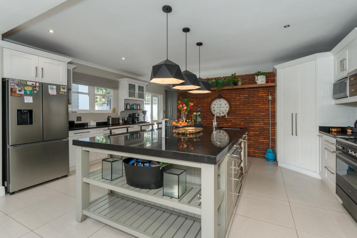 Modern kitchen featuring a large central island with granite countertops, exposed brick feature wall, ample cabinetry, and high-quality built-in appliances.