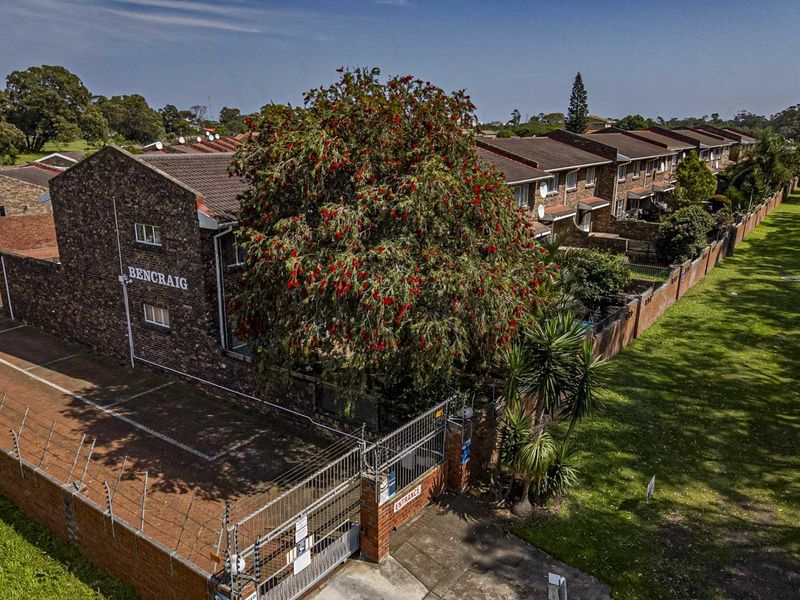 Aerial view of the Bencraig townhouse complex, showcasing the brick exterior, tiled roofing, perimeter security fencing, and paved driveway entrance.