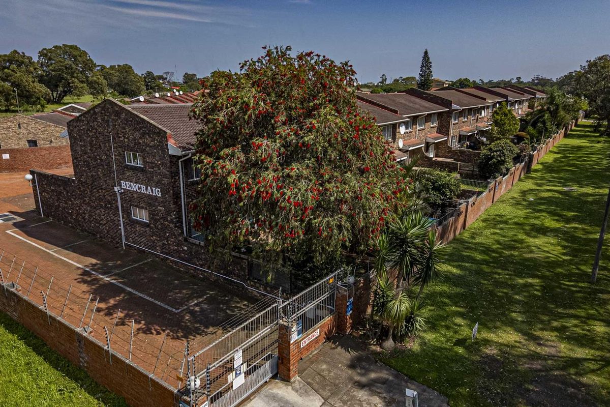 Aerial view of the Bencraig townhouse complex, showcasing the brick exterior, tiled roofing, perimeter security fencing, and paved driveway entrance.
