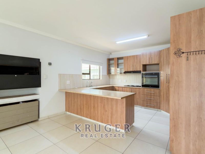 Spacious open-plan kitchen featuring wood-look cabinetry, built-in appliances, and a breakfast bar, seamlessly flowing into a living area with a built-in fireplace.