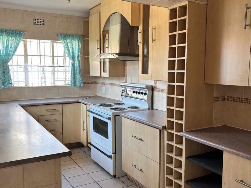 A functional kitchen featuring light wood-tone cabinetry, laminate countertops, a built-in extractor fan, and a freestanding electric stove with tiled flooring.