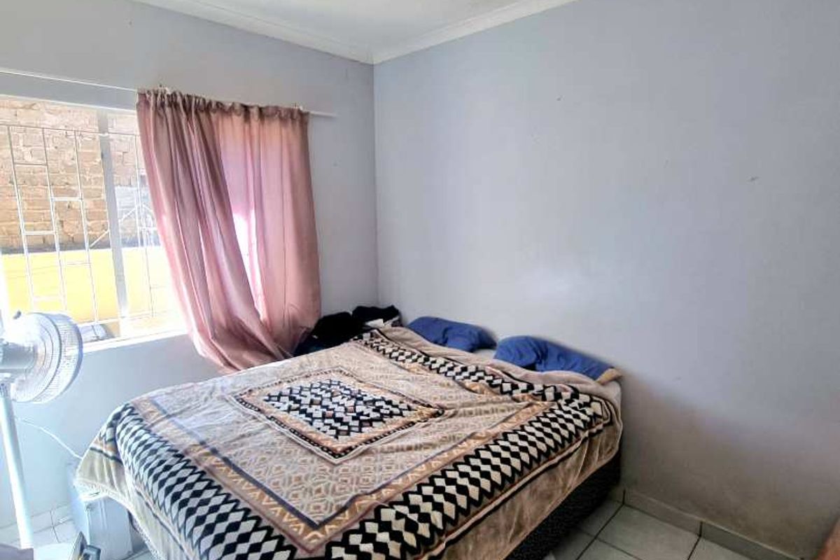 A bedroom featuring tiled flooring and security burglar bars on the window, currently showing signs of wear on the ceiling and walls.