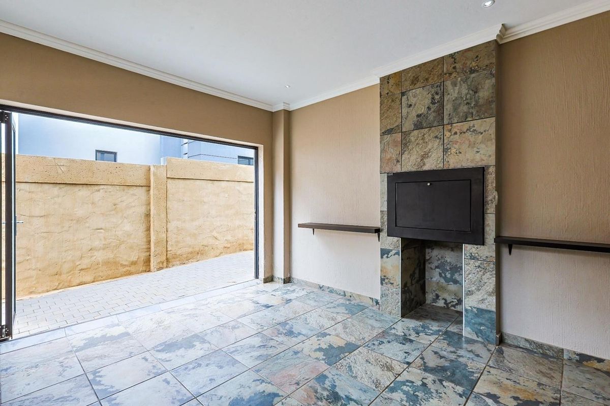 An open-plan living area featuring a built-in fireplace with stone cladding, tiled flooring, and large sliding doors opening to an outdoor paved area.