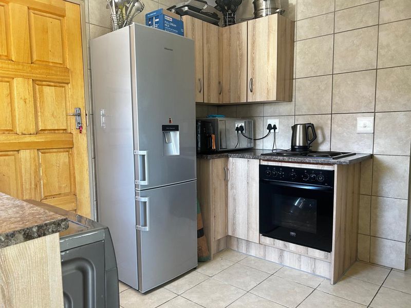 Compact kitchen featuring light wood-finish cabinetry, dark laminate countertops, built-in oven, electric hob, and neutral wall tiling.
