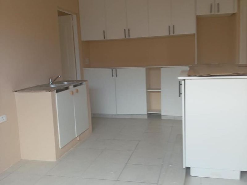 An unfinished kitchen space featuring white built-in cabinetry, a double sink, and tiled flooring, currently awaiting final countertop installation and completion.