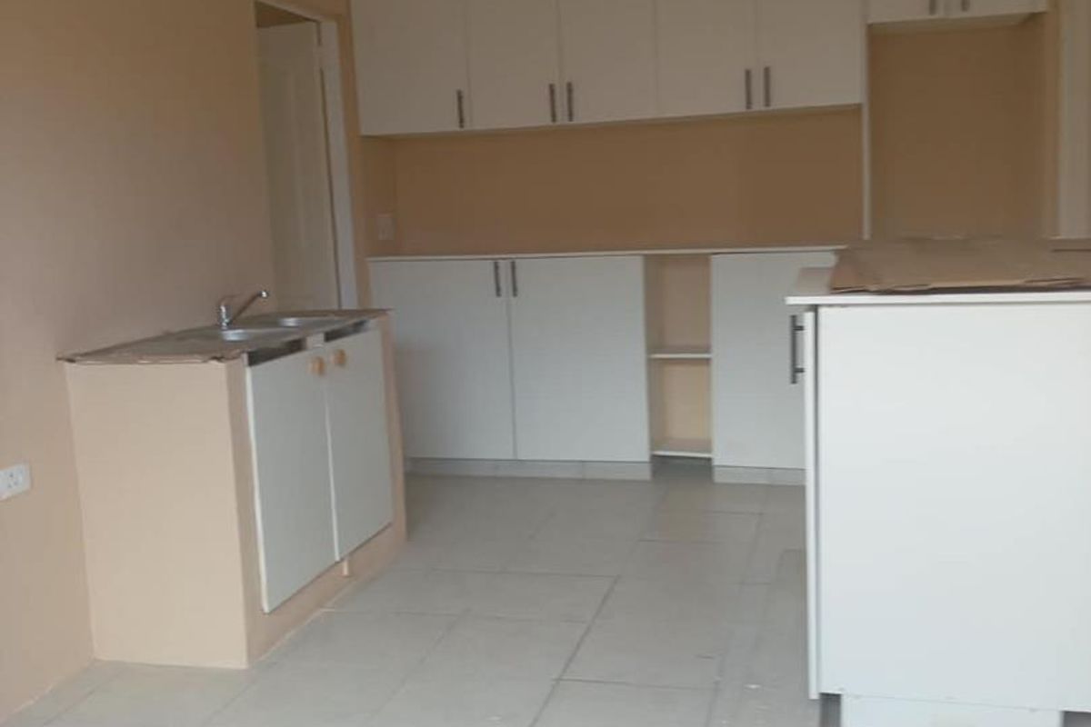 An unfinished kitchen space featuring white built-in cabinetry, a double sink, and tiled flooring, currently awaiting final countertop installation and completion.