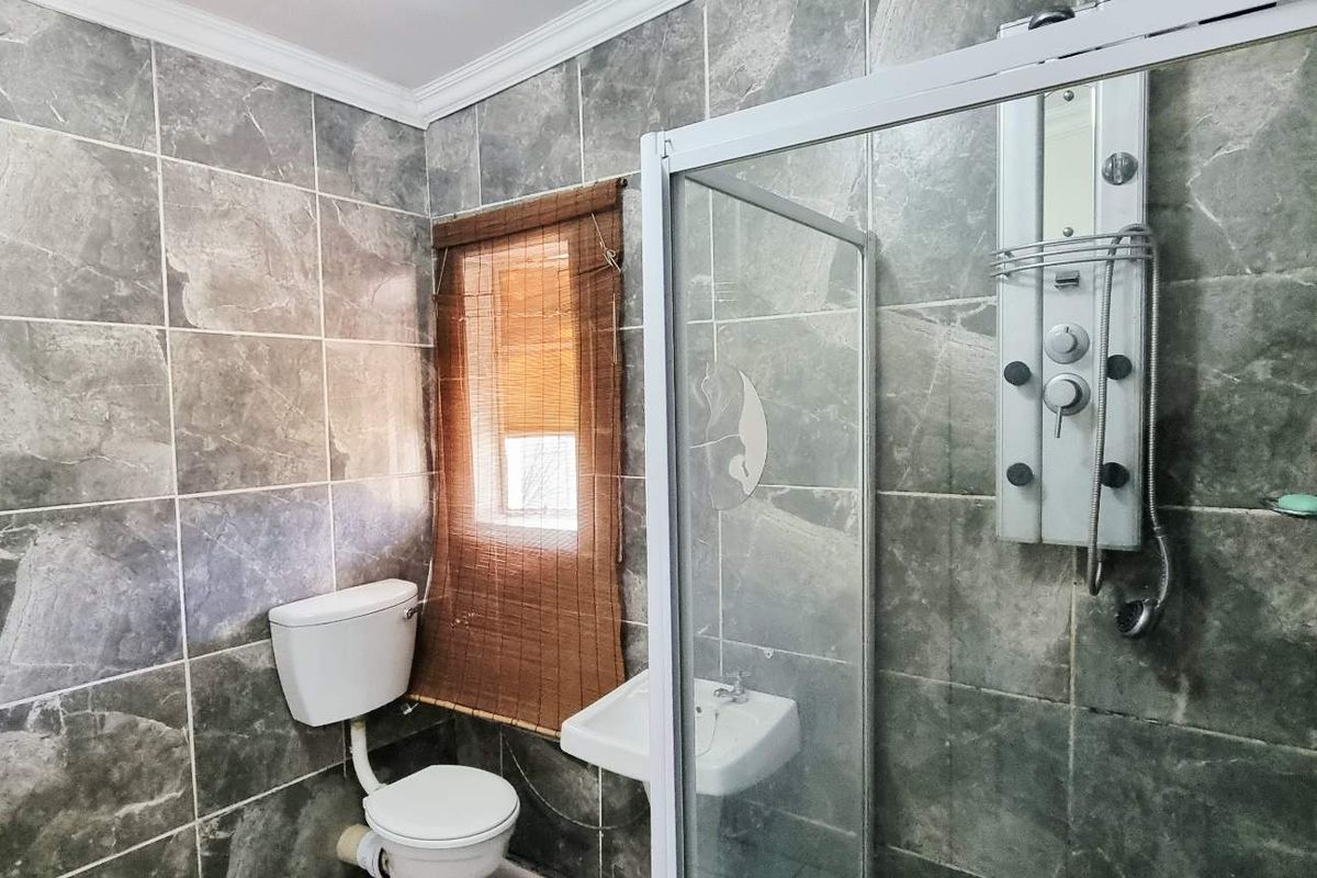 A functional bathroom featuring full-height grey stone-look wall tiles, a glass shower enclosure with a multi-jet shower panel, a toilet, and a wall-mounted basin.