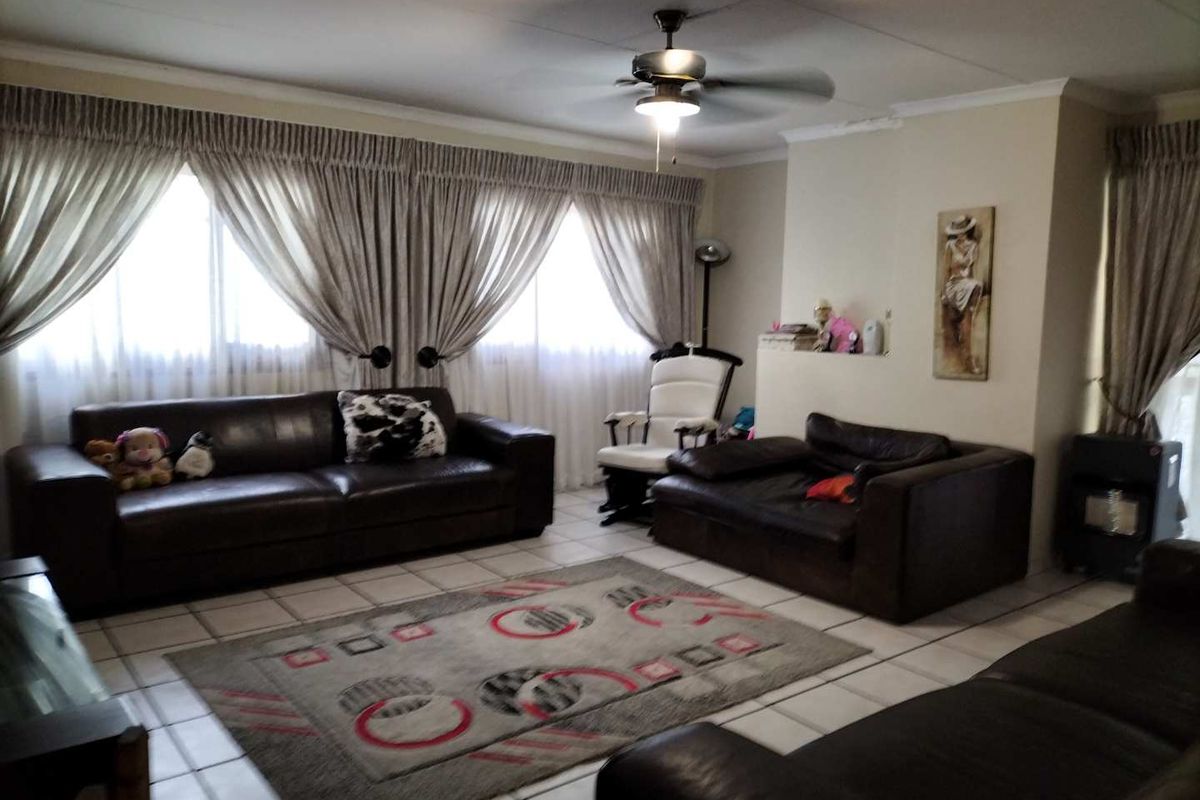Spacious living room featuring tiled flooring, a central ceiling fan, and large windows with curtain treatments.