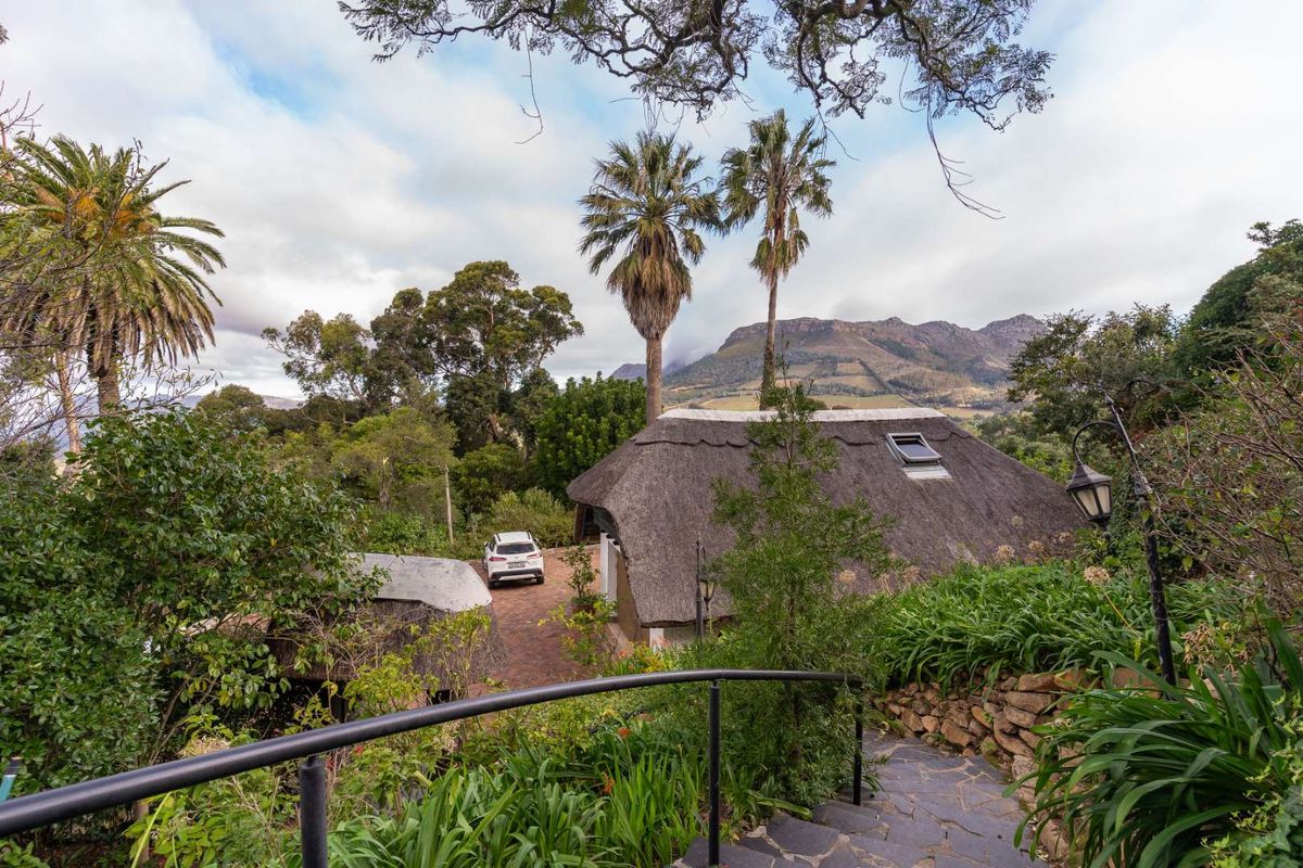 Elevated view of a thatched-roof property set within a lush, landscaped garden with mountain vistas in the background.