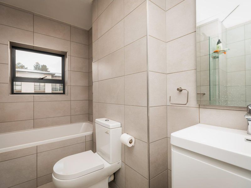 A modern, neutral-toned bathroom featuring a bathtub, toilet, and vanity with a basin, finished with floor-to-ceiling wall tiles.