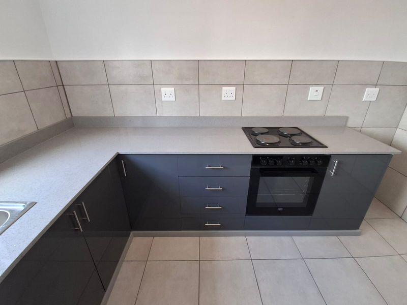 Modern kitchen featuring sleek grey cabinetry, stone countertops, a built-in electric oven and hob, and neutral tiled finishes.