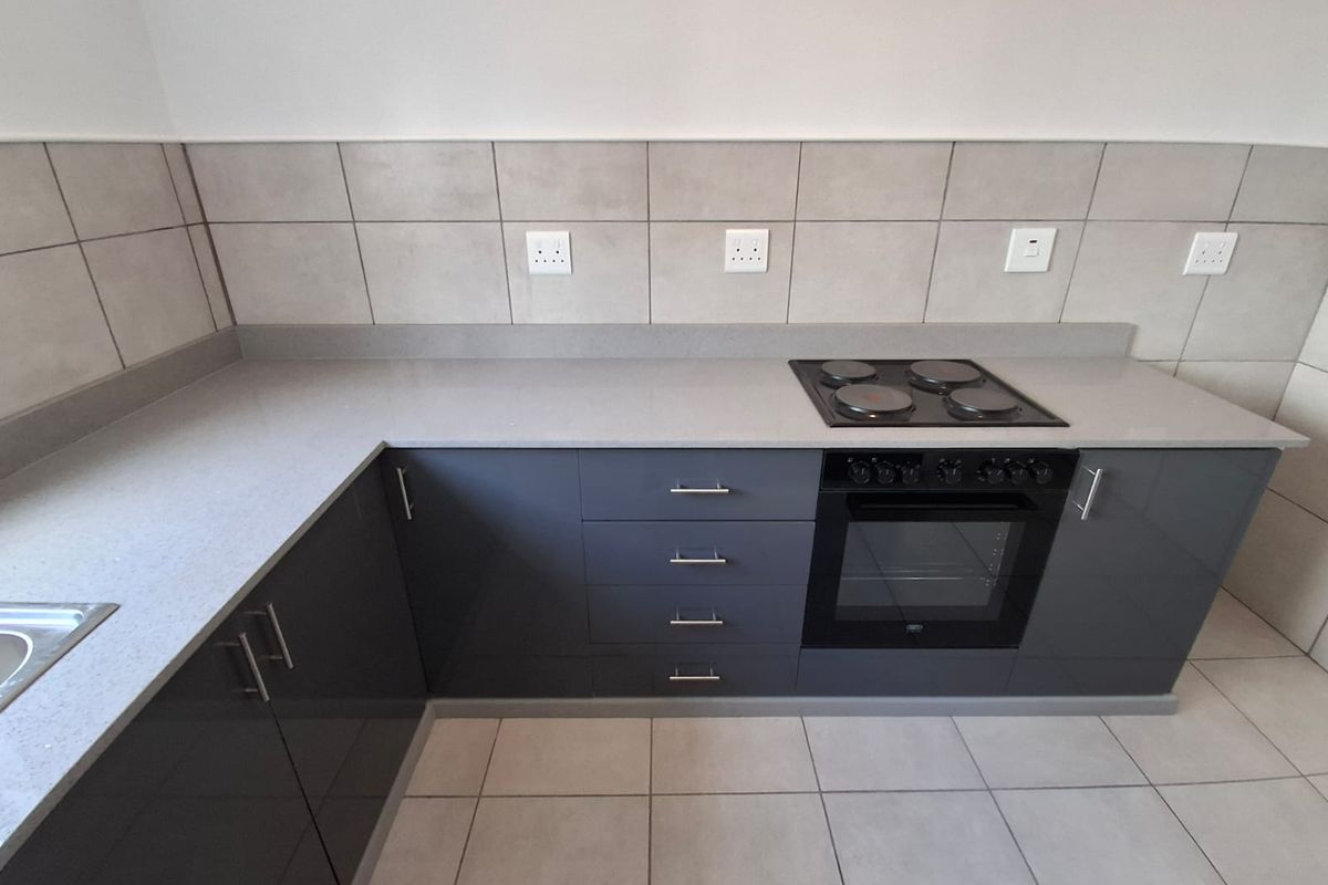 Modern kitchen featuring sleek grey cabinetry, stone countertops, a built-in electric oven and hob, and neutral tiled finishes.