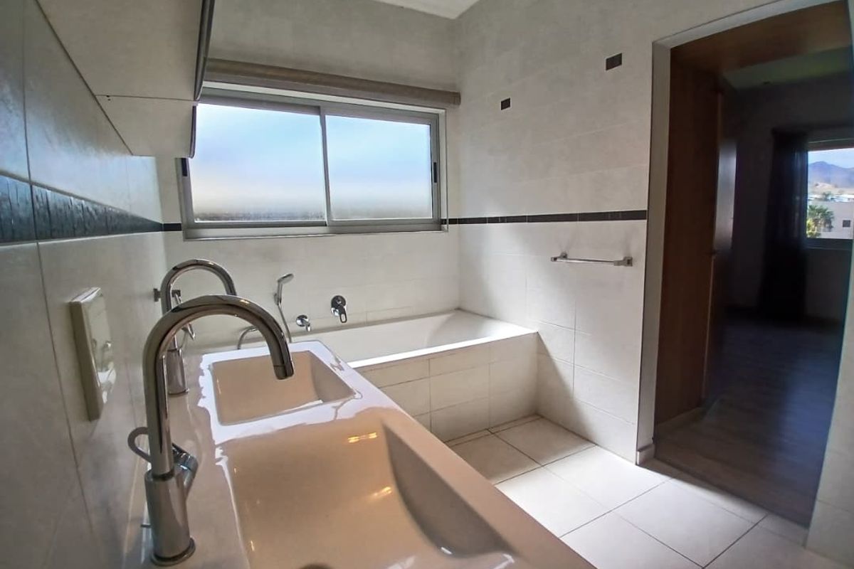 A clean, modern bathroom featuring a built-in bathtub, double vanity sink with chrome fixtures, and neutral tiled finishes throughout.