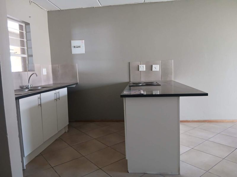 A functional kitchen featuring white cabinetry, dark laminate countertops, an integrated electric hob, and neutral tiled flooring in an open-plan layout.